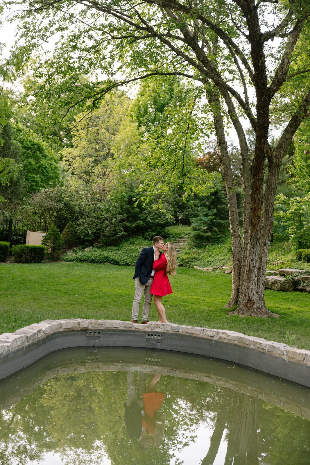 Sydney, in a red dress, kissing Trenton beside the reflecting pond.